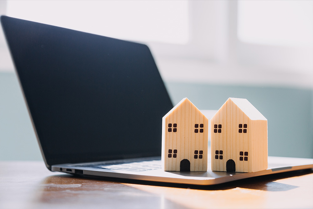 Verwaltung von Immobilien - Holzmodell-Häuser platziert auf einem Laptop